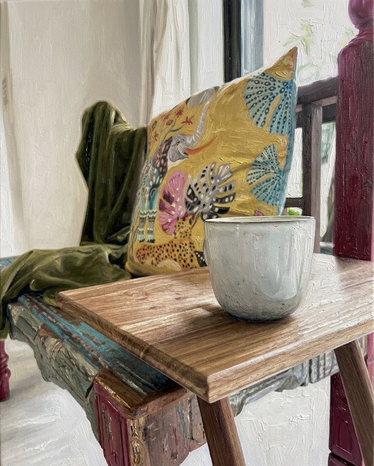 Oil still-life painting — a patterned cushion and stone cup resting on a rustic wooden bench
